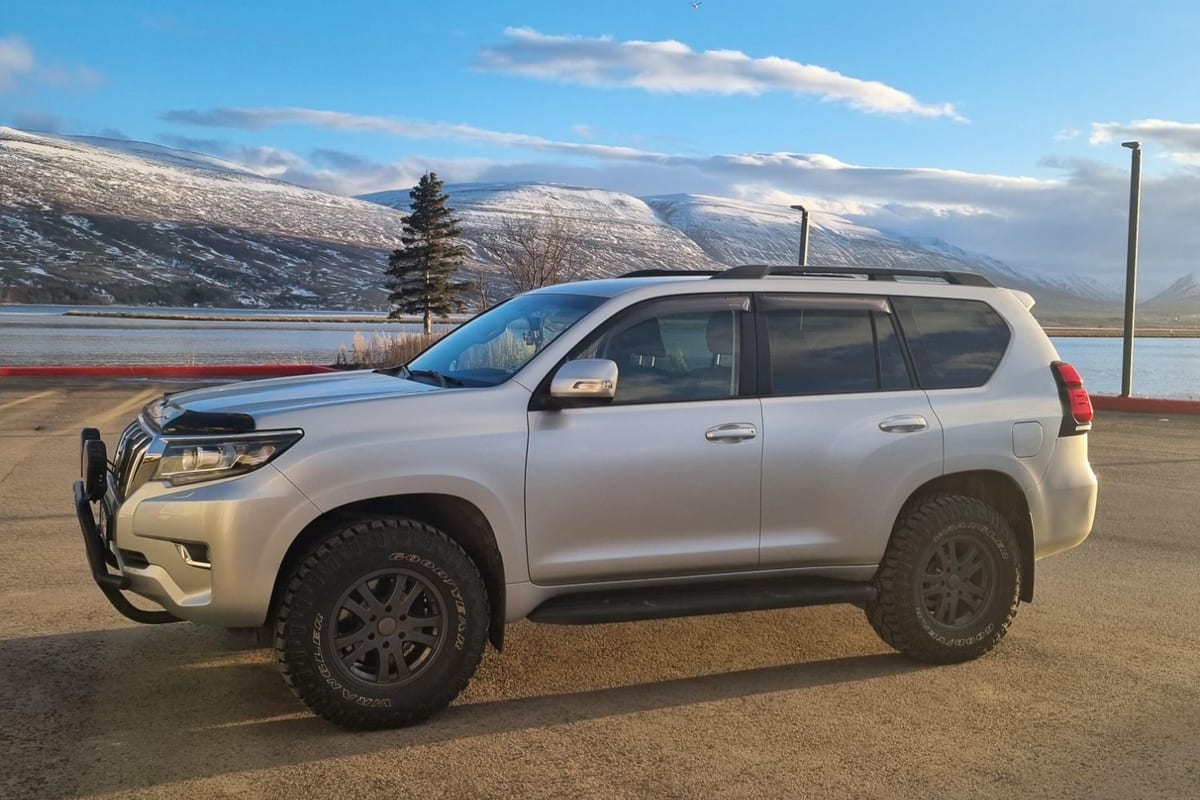 Silfurlitaður jeppi Jóns við fjörð með snævi þakin fjöll í bakgrunni