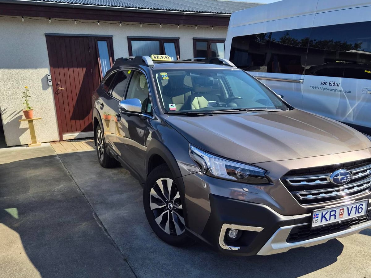 Leigubíll Jóns með TAXI-skilti og rútan merkt Jón Eiður í bakgrunni